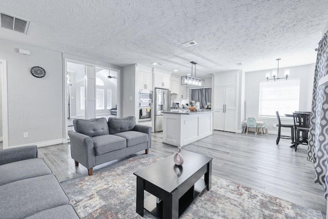 living room with light wood-type flooring, an inviting chandelier, visible vents, and a textured ceiling