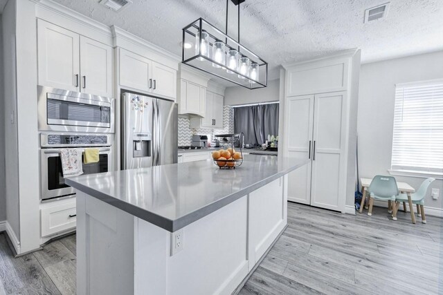 kitchen with light wood finished floors, visible vents, appliances with stainless steel finishes, a center island, and white cabinetry