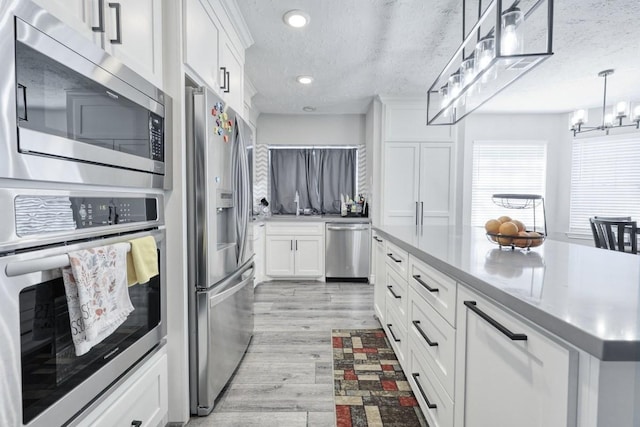 kitchen with stainless steel appliances, white cabinetry, light wood-style flooring, and a textured ceiling