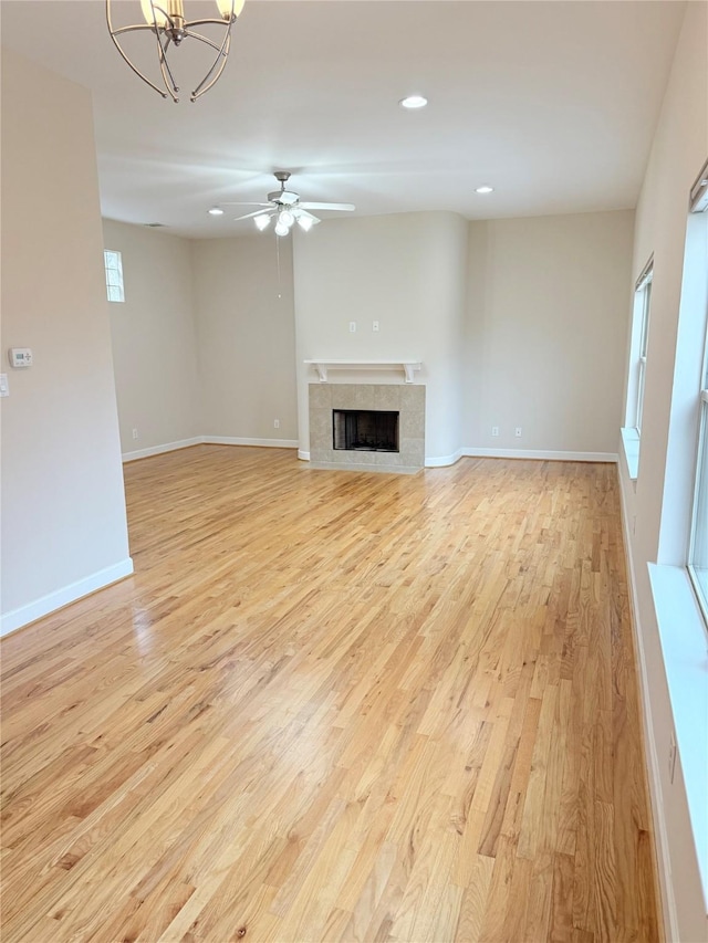 unfurnished living room with ceiling fan with notable chandelier, a tile fireplace, and light hardwood / wood-style flooring