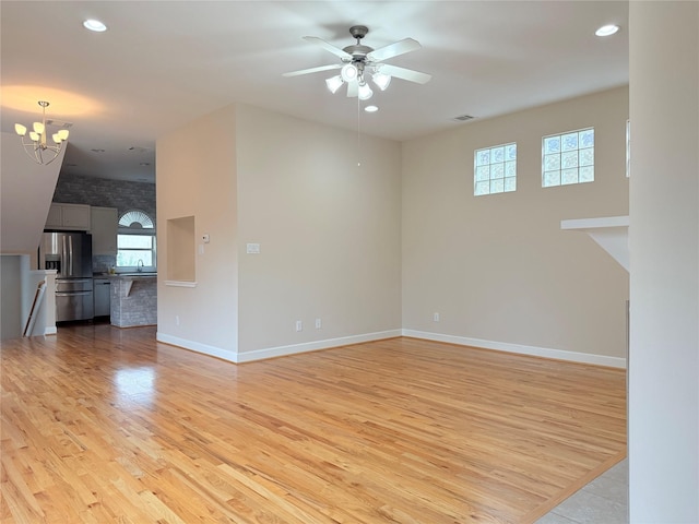 empty room with plenty of natural light, sink, ceiling fan with notable chandelier, and light hardwood / wood-style floors