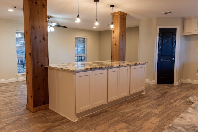 kitchen with ceiling fan, hanging light fixtures, light stone counters, wood-type flooring, and white cabinets