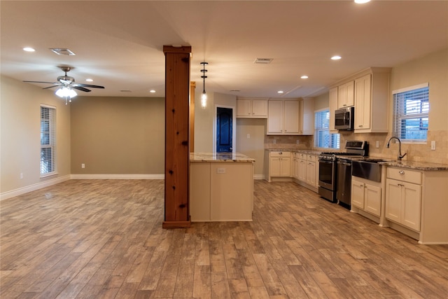 kitchen with appliances with stainless steel finishes, light stone countertops, light hardwood / wood-style floors, white cabinets, and decorative light fixtures