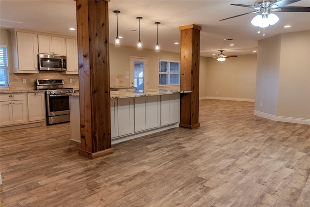 kitchen with pendant lighting, light hardwood / wood-style flooring, light stone countertops, and appliances with stainless steel finishes