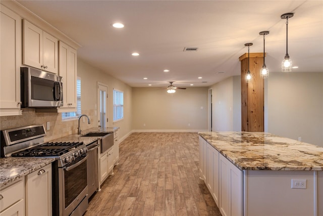 kitchen with white cabinetry, light stone counters, a center island, and appliances with stainless steel finishes