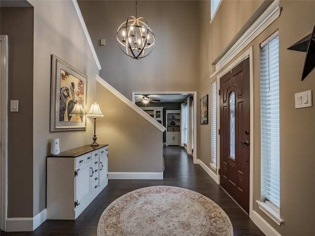 foyer entrance with a high ceiling, ornamental molding, ceiling fan with notable chandelier, and dark hardwood / wood-style flooring