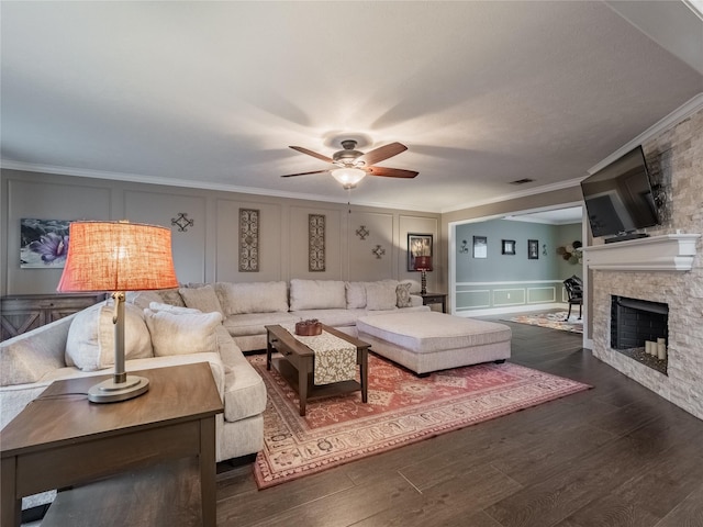 living room featuring dark hardwood / wood-style floors, ceiling fan, ornamental molding, and a stone fireplace