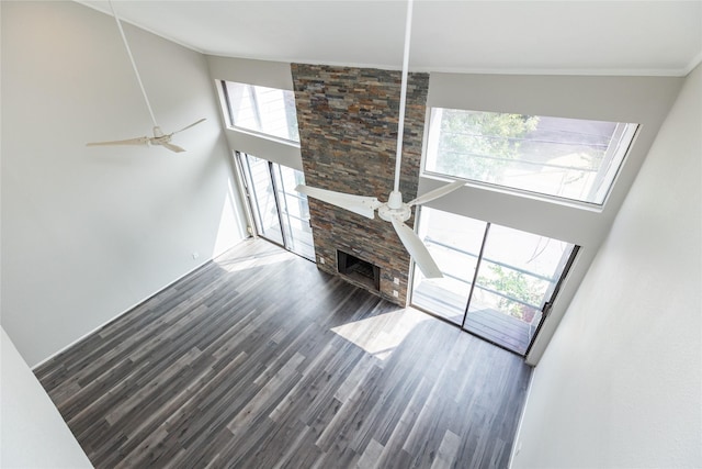 unfurnished living room featuring a high ceiling, a stone fireplace, dark hardwood / wood-style floors, and ceiling fan