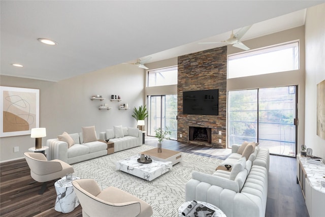 living room featuring dark hardwood / wood-style flooring, a stone fireplace, ceiling fan, and a high ceiling