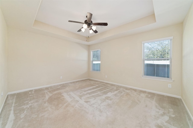 carpeted spare room with a tray ceiling and ceiling fan