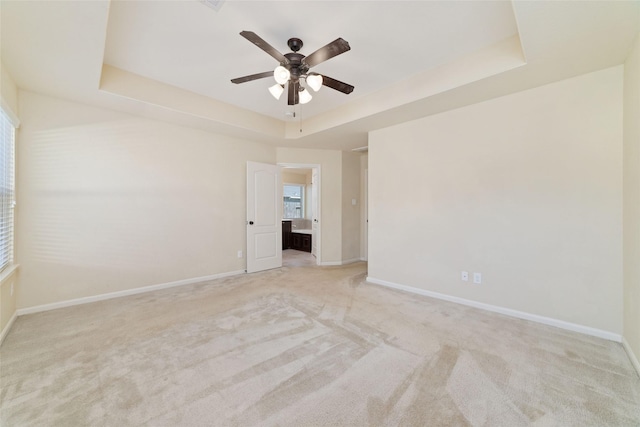 empty room with ceiling fan, a tray ceiling, and light carpet