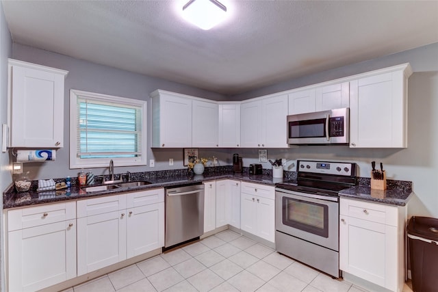 kitchen with white cabinetry, stainless steel appliances, sink, and dark stone counters