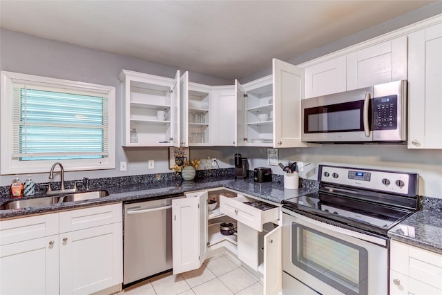 kitchen featuring sink, light tile patterned floors, appliances with stainless steel finishes, dark stone countertops, and white cabinets