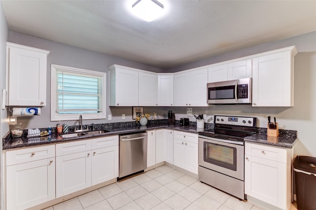 kitchen with sink, white cabinetry, light tile patterned floors, appliances with stainless steel finishes, and dark stone counters