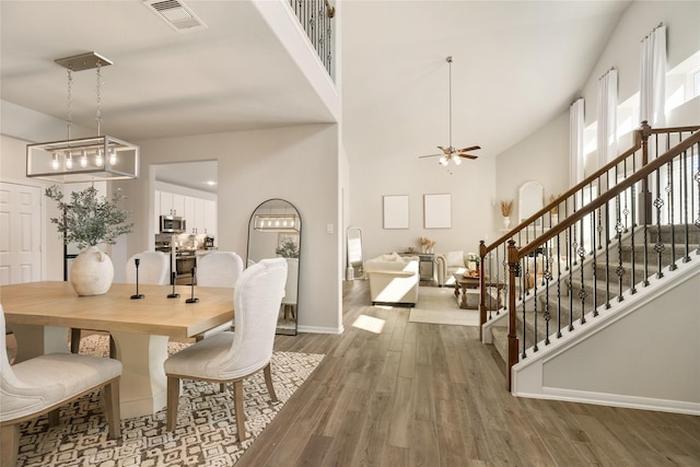 dining space with hardwood / wood-style flooring, ceiling fan with notable chandelier, and a high ceiling