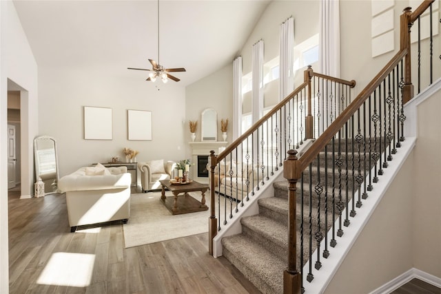 stairs with ceiling fan, a towering ceiling, and wood-type flooring