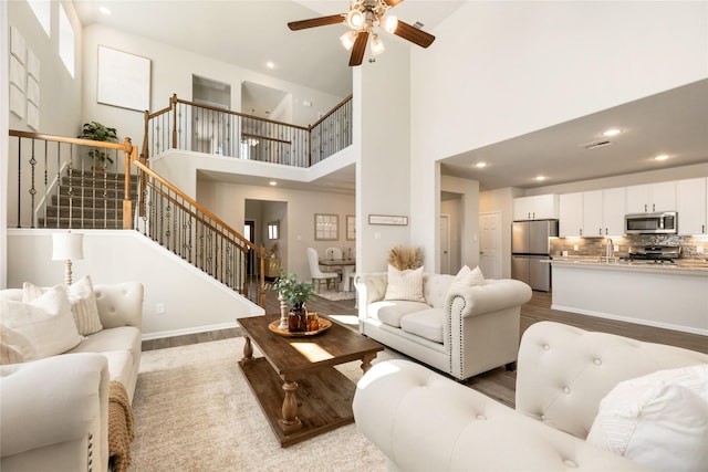 living room featuring ceiling fan, sink, a high ceiling, and light wood-type flooring