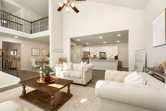 living room featuring ceiling fan, a high ceiling, and light wood-type flooring