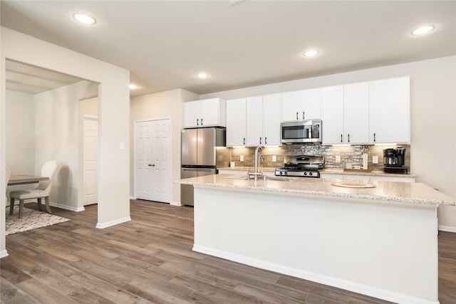 kitchen featuring white cabinetry, appliances with stainless steel finishes, light stone countertops, and a center island with sink