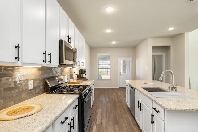 kitchen with sink, white cabinetry, backsplash, stainless steel appliances, and light stone counters