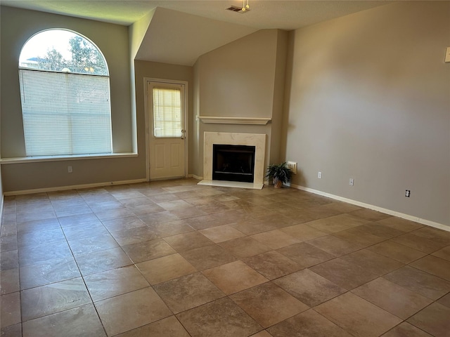 unfurnished living room with a wealth of natural light, a high end fireplace, and vaulted ceiling