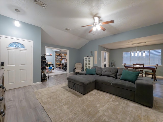 living room with lofted ceiling, a textured ceiling, light hardwood / wood-style flooring, and ceiling fan