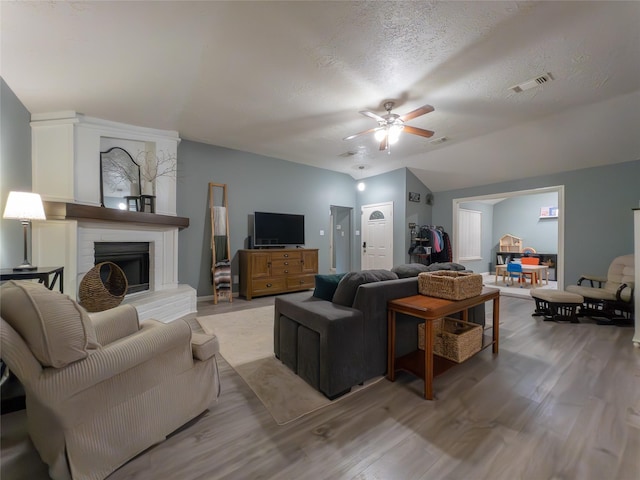 living room with lofted ceiling, a textured ceiling, hardwood / wood-style flooring, ceiling fan, and a fireplace