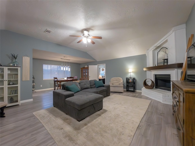 living room featuring lofted ceiling, wood-type flooring, a brick fireplace, a textured ceiling, and ceiling fan