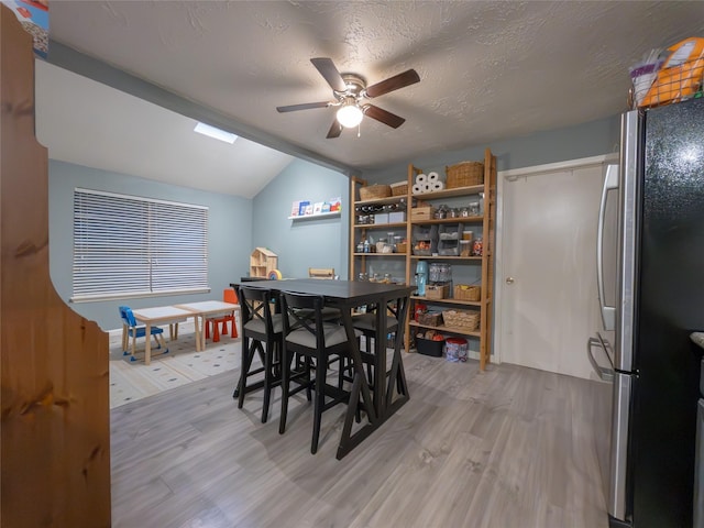 dining area featuring ceiling fan, vaulted ceiling, a textured ceiling, and light wood-type flooring