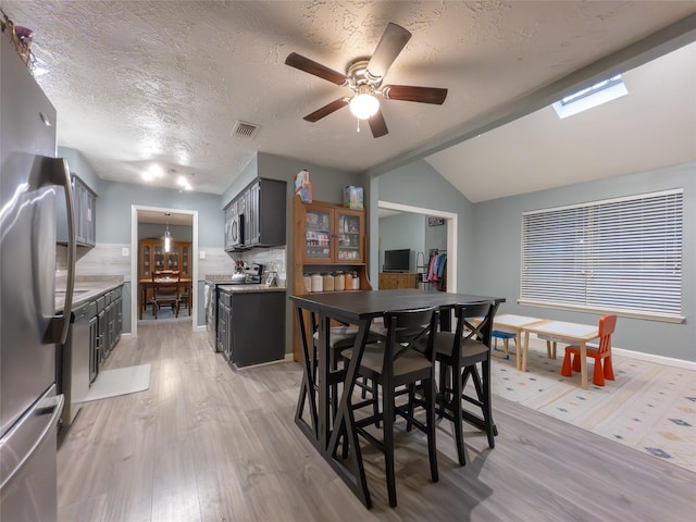 dining room with ceiling fan, vaulted ceiling, a textured ceiling, and light wood-type flooring