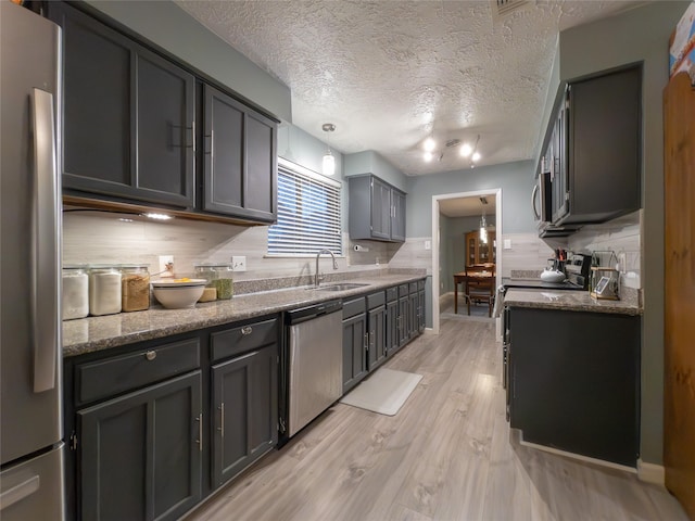 kitchen with sink, tasteful backsplash, hanging light fixtures, light wood-type flooring, and stainless steel appliances