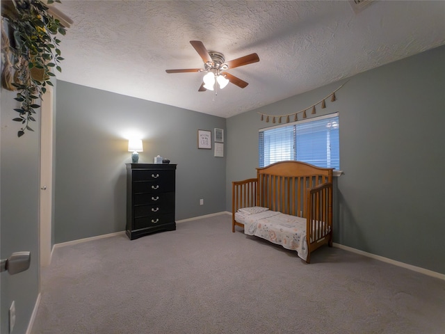 carpeted bedroom featuring ceiling fan, a crib, and a textured ceiling