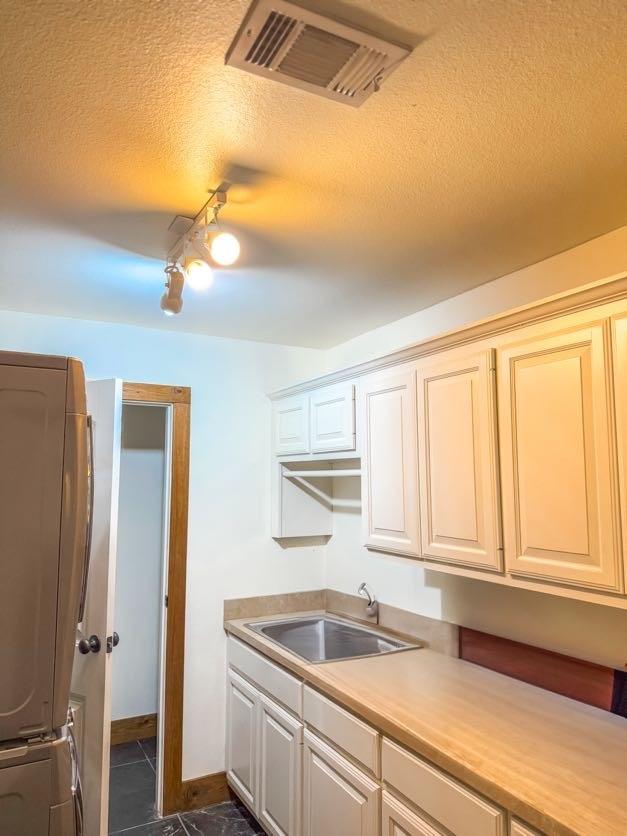 kitchen featuring sink, stacked washer / drying machine, dark tile patterned flooring, and a textured ceiling