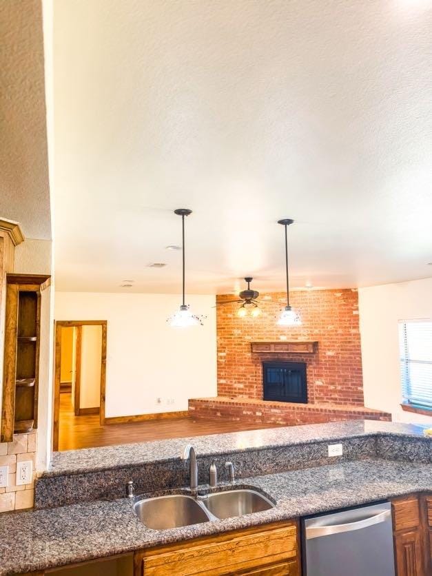 kitchen with sink, ceiling fan, hanging light fixtures, a fireplace, and stainless steel dishwasher