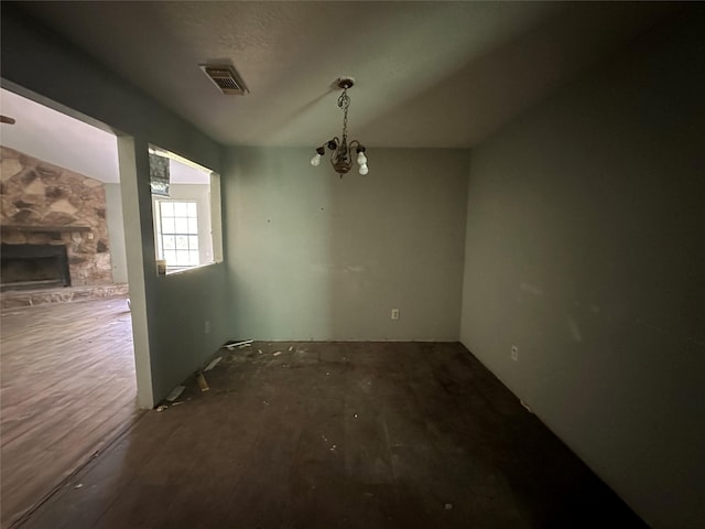 unfurnished dining area featuring a stone fireplace and a chandelier