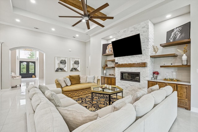 tiled living room with crown molding, a fireplace, a raised ceiling, and a high ceiling