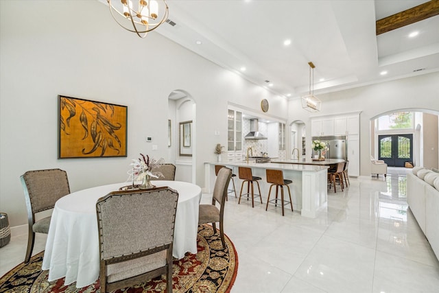 dining space with french doors, sink, a notable chandelier, a towering ceiling, and beam ceiling