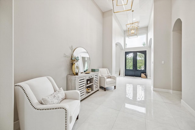 foyer with a high ceiling, light tile patterned flooring, a notable chandelier, and french doors