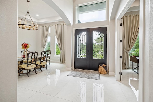 tiled entrance foyer with a notable chandelier, a tray ceiling, and french doors