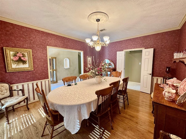 dining room with ornamental molding, a chandelier, light hardwood / wood-style flooring, and a textured ceiling