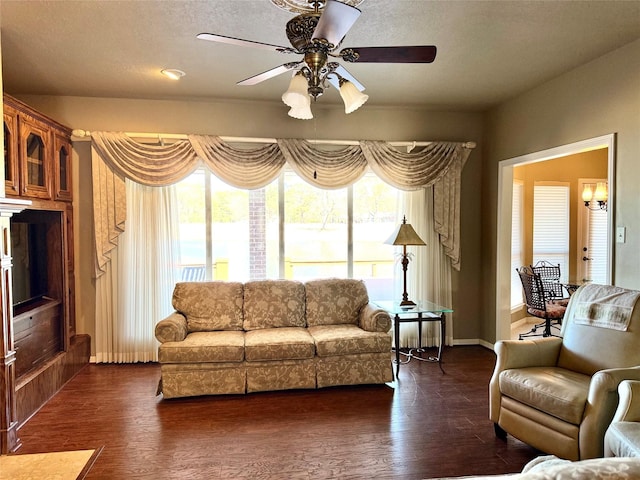 living area featuring baseboards, a ceiling fan, dark wood-type flooring, and a wealth of natural light