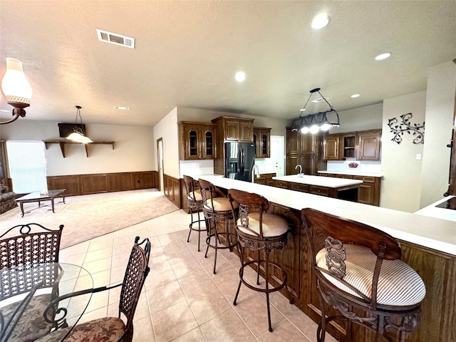 kitchen with a center island, stainless steel refrigerator with ice dispenser, visible vents, light countertops, and wainscoting