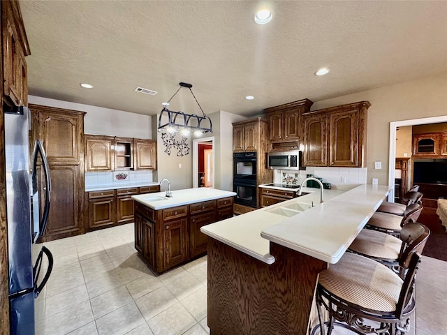 kitchen with a kitchen island with sink, a sink, light countertops, appliances with stainless steel finishes, and pendant lighting