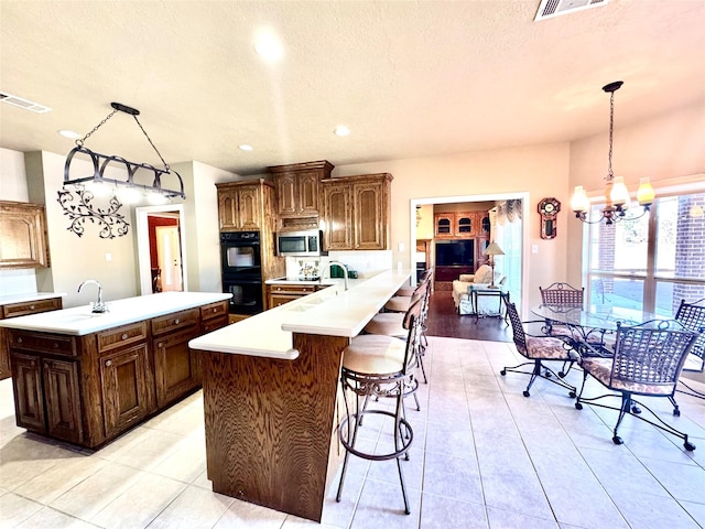 kitchen with visible vents, stainless steel microwave, a peninsula, hanging light fixtures, and light countertops