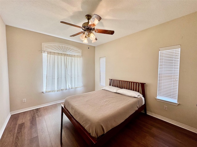 bedroom featuring multiple windows, dark wood-style flooring, a ceiling fan, and baseboards