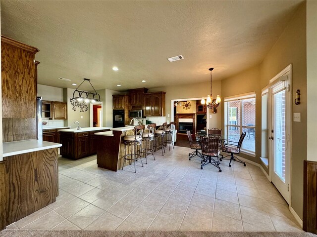 kitchen featuring refrigerator, a chandelier, hanging light fixtures, light tile patterned floors, and an island with sink