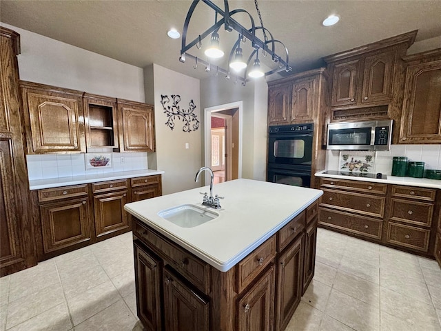 kitchen with sink, hanging light fixtures, tasteful backsplash, black appliances, and a center island with sink