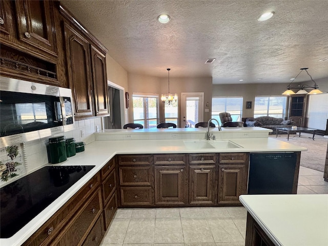 kitchen featuring light countertops, open floor plan, a sink, a peninsula, and black appliances