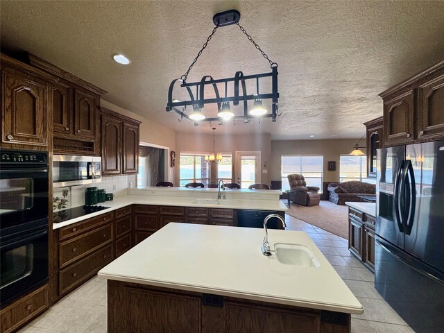 kitchen with a kitchen island with sink, sink, hanging light fixtures, and black appliances