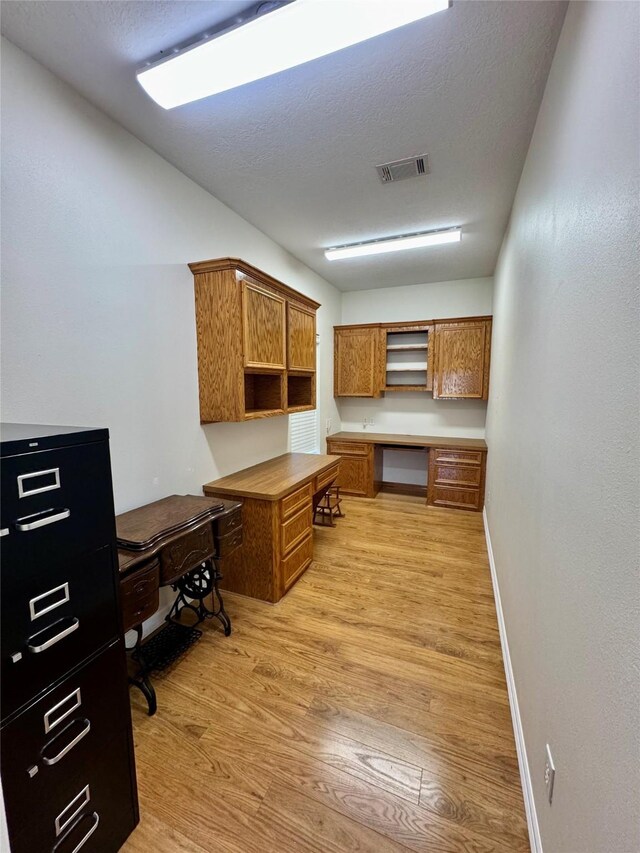 home office with built in desk, a textured ceiling, and light wood-type flooring